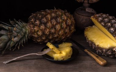 Bıçak ve arkasında bütün ananas ile eski rustik masada Dilimlenmiş ananas. Siyah arka plan.