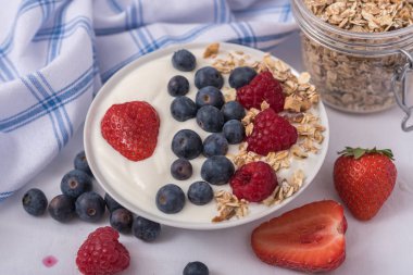 Beyaz arka plan üzerinde yulaf ezmesi ve çilek, yaban mersini ve ahududu ile kase beyaz yoğurt.