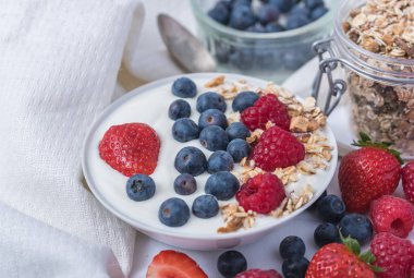 Beyaz arka plan üzerinde yulaf ezmesi ve çilek, yaban mersini ve ahududu ile kase beyaz yoğurt.