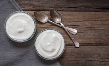 Yanında iki kaşık ile eski ahşap masada iki cam kase beyaz yoğurt.