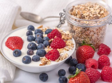 Beyaz arka plan üzerinde yulaf ezmesi ve çilek, yaban mersini ve ahududu ile kase beyaz yoğurt.