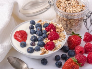 Beyaz arka plan üzerinde yulaf ezmesi ve çilek, yaban mersini ve ahududu ile kase beyaz yoğurt.