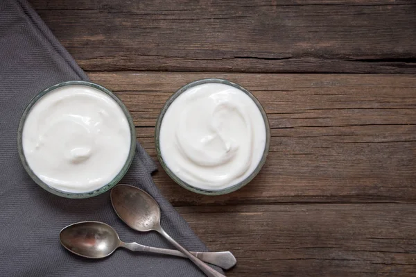 Yogurt putih dalam dua mangkuk kaca di meja kayu tua dengan dua sendok di sebelah . — Stok Foto