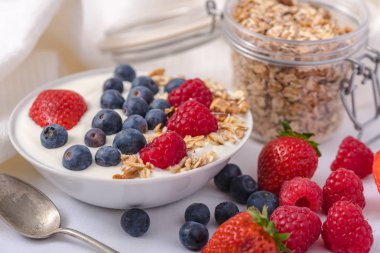 Beyaz arka plan üzerinde yulaf ezmesi ve çilek, yaban mersini ve ahududu ile kase beyaz yoğurt.