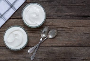 Eski rustik kaşık ile eski ahşap masada cam kase beyaz yoğurt.