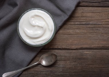 Eski rustik kaşık ile eski ahşap masada cam kase beyaz yoğurt.