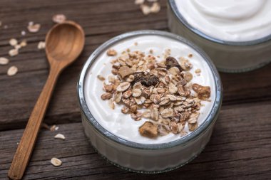 Eski ahşap kaşık ve yulaf ezmesi ile eski ahşap masada cam kase beyaz yoğurt.