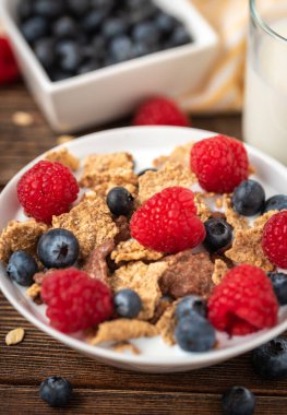 Böğürtlenli mısır gevreği ve ahududu, beyaz kasede, siyah ahşap masada..