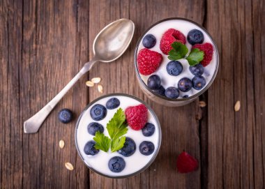 İki kasede yaban mersinli beyaz yoğurt, ahududulu doğal ahşap masa, düz manzara..