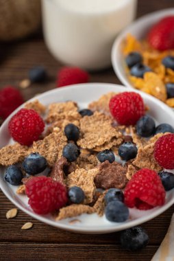 Böğürtlenli mısır gevreği ve ahududu, siyah ahşap masada beyaz kasede..