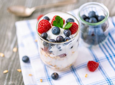 Cam kavanozda beyaz yoğurt ve gri arka planda meyveler..