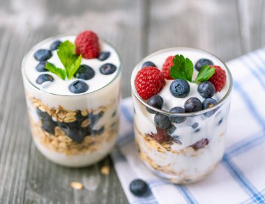 Cam kavanozda beyaz yoğurt ve gri arka planda meyveler..