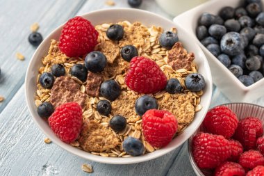 Böğürtlenli granola ve beyaz kaseli ahududu koyu beyaz masa.