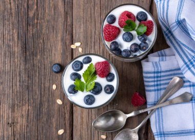 Doğal ahşap masa üzerinde yaban mersini ve ahududu içeren iki kâse beyaz yoğurt..