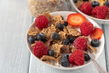 Böğürtlenli granola ve beyaz kaseli ahududu koyu beyaz masa.