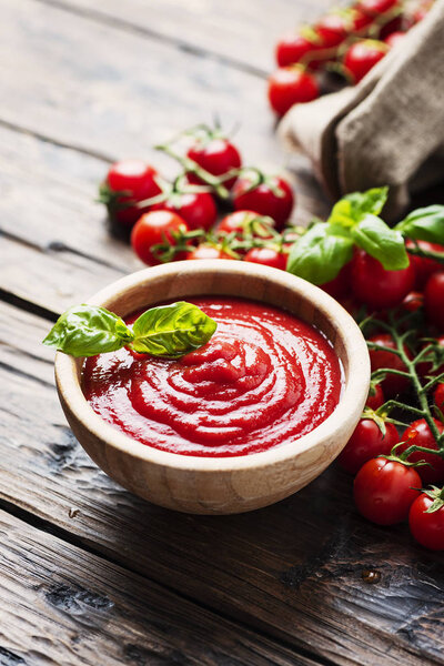 Bowl of tomato sauce and cherry tomatoes on wooden table