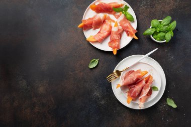 Tatlı kavun ve koyu arkaplanlı jambonlu yaz aperatifi. Kopyalama alanı olan en üst görüntü