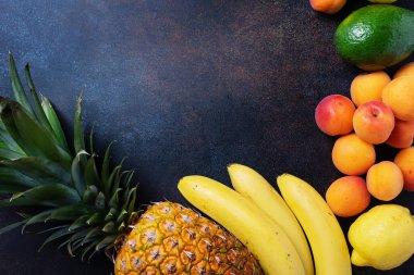Sağlıklı vejetaryen yemeği kavramı. Ananas, muz, kayısı, kavun, siyah arka planda avokado. En üst görüntü