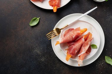 Tatlı kavun ve koyu arkaplanlı jambonlu yaz aperatifi. Kopyalama alanı olan en üst görüntü