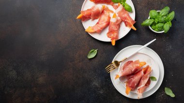 Tatlı kavun ve koyu arkaplanlı jambonlu yaz aperatifi. Kopyalama alanı ve kaydırma biçimi olan en üstteki görüntü