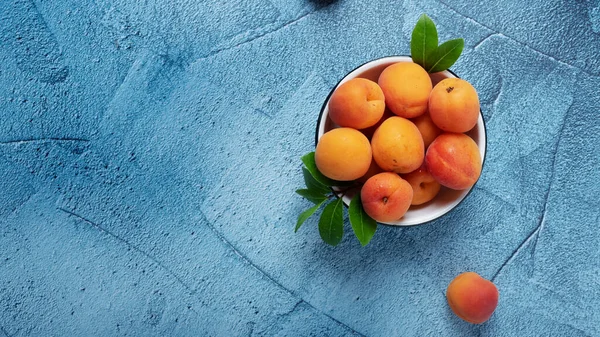 Sweet fresh apricots in the white bowl on the blue back ground. Top view image with copy space, slider format