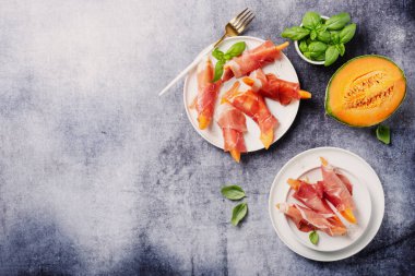 Tatlı kavun ve koyu arkaplanlı jambonlu yaz aperatifi. Kopyalama alanı olan en üst görüntü