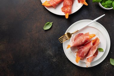 Tatlı kavun ve koyu arkaplanlı jambonlu yaz aperatifi. Kopyalama alanı olan en üst görüntü