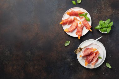 Tatlı kavun ve koyu arkaplanlı jambonlu yaz aperatifi. Kopyalama alanı olan en üst görüntü