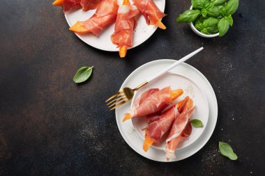 Tatlı kavun ve koyu arkaplanlı jambonlu yaz aperatifi. Kopyalama alanı olan en üst görüntü