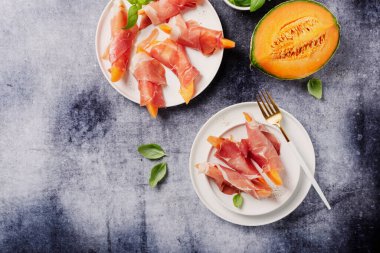 Tatlı kavun ve koyu arkaplanlı jambonlu yaz aperatifi. Kopyalama alanı olan en üst görüntü