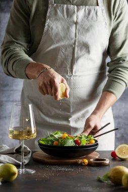 Kırmızı ve sarı domatesli sağlıklı yeşil salata için limon sıkan adam, seçici odak görüntüsü