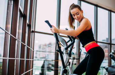 Genç ve çekici bir kadın spor salonunda kardiyo eğitimi alıyor..