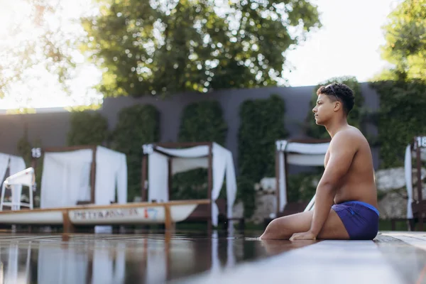 Genç Latin yüzücü, sıkı bir eğitimden sonra havuz kenarında derin derin oturur ve biraz dinlenir.