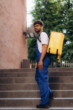 Kurye, izole edilmiş bir termal sırt çantasında yiyecek taşırken merdivenleri tırmanıyor ve kentsel bir ortamda etkin hizmet veriyor.