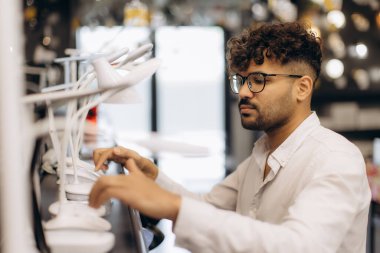 Masa lambalarının kalitesini ve işlevselliğini iyi aydınlatılmış modern aydınlatma mağazası ortamında inceleyen bir kişi.