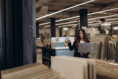 Ev geliştirme mağazasında dizüstü bilgisayarla tablet örneklerini inceleyen profesyonel bir kadın..