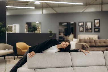 Zarif bir kadın modern, rahat bir kanepeye uzanıyor modern bir mobilya galerisinde sofistike dekorlu ve sıcak ışıklandırmalı, misafirperver ve sade bir ortam yaratıyor..