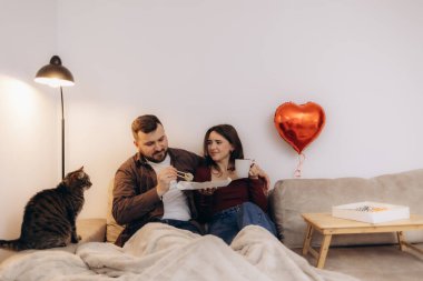 Sevgi dolu bir çiftin kedi, kırmızı kalp balonu, kahve ve atıştırmalıklarla rahatladığı sıcak bir sahne..