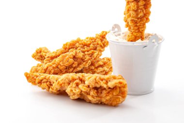 Fast food ve protein yüksek beslenme konsepti ile altın ekmekli tavuk şeritleri ve beyaz arka planda izole edilmiş metal bir çiftlik sosu kovasına batırılmış çıtır bir şerit yemek.