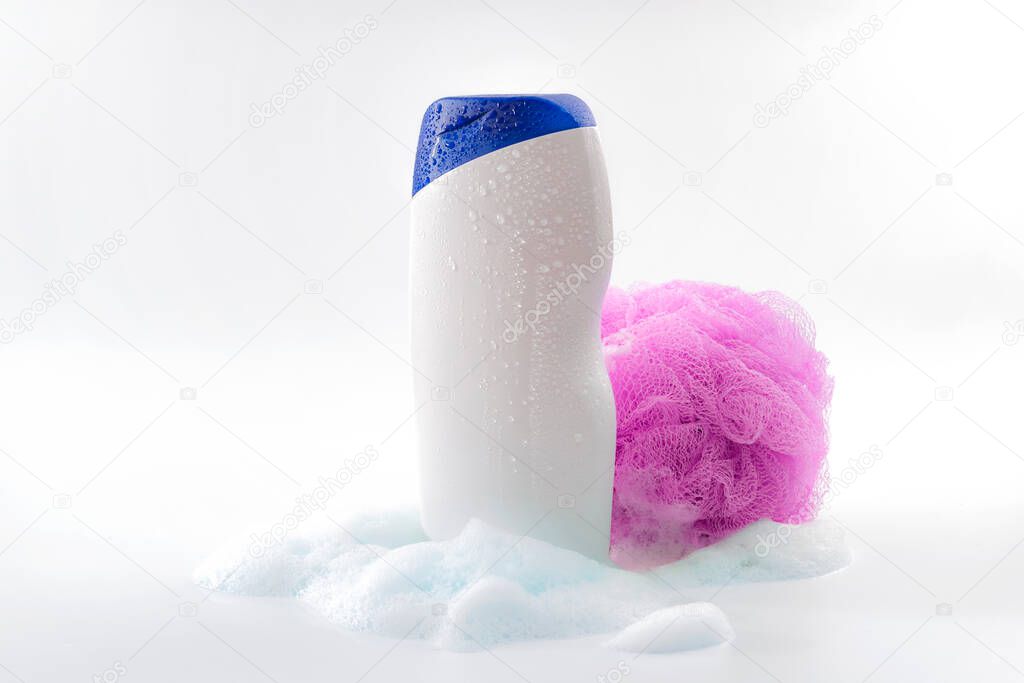 Personal hygiene, daily routine and body care toiletries concept theme with a bottle of shower gel soaked in water drops, bubbles made by soap foam and pink shower sponge isolated on white background