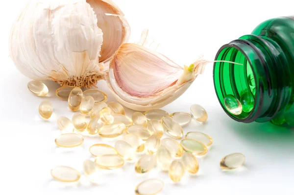 Alternative medicine, supplements for illness prevention and immune system boost concept with garlic and allicin gel capsules and green pill bottle isolated on white background