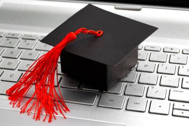 İnternet akademik öğrenme, e-öğrenme ve çevrimiçi kolej eğitimi konsepti teması. Mezuniyet şapkasına yakın çekimde bilgisayar klavyesinde kırmızı püsküllü.