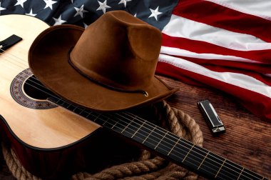 Amerikan kültürü, kovboy şapkası, Amerikan bayrağı, akustik gitar, mızıka ve eski bir salonun ahşap arka planında bir ip kementle yaşayan bir çiftlik ve ülke muisc konsepti teması.