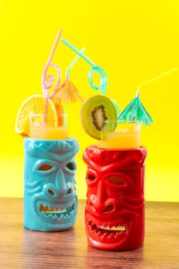 Hawaii tiki barı, yaz ferahlatıcı içecekler ve alkol ve meyve suyu bardaklarıyla karıştırılmış tropikal kokteyl konsepti teması, kivi ve portakal dilimleri, şemsiye ve ahşap masada pipet içmek.