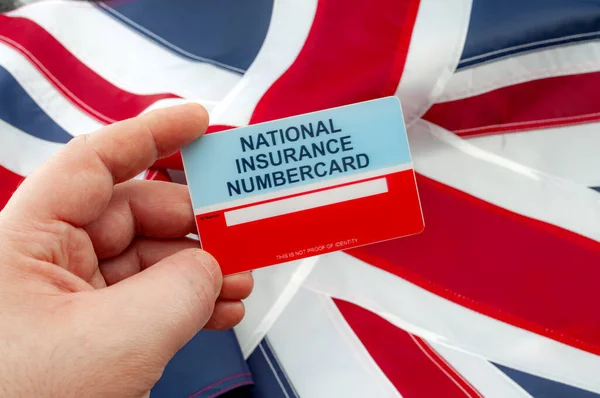 Social security system, access to safety net programs in Great Britain concept theme with a blank National Insurance Number card or NINO held in one hand with the UK flag in the background