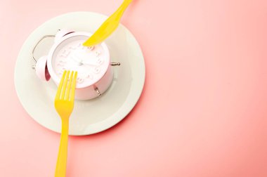 Kilo kaybı stratejisi metaforu ve aralıklı oruç planı konsepti, boş tabakta en az saat fotoğrafçılığı ve parlak sarı çatal ve bıçak ile fotokopi alanı ile izole edilmiş pembe arka plan.