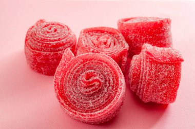 Çiğnenmiş tatlılar, çilek ve vişne aromalı şekerleme kavramı. Tatlı ve ekşi ekşi kırmızı ekşi kemerlerin üzerine yakın çekim. Pembe arka planda izole edilmiş şeker kaplı.