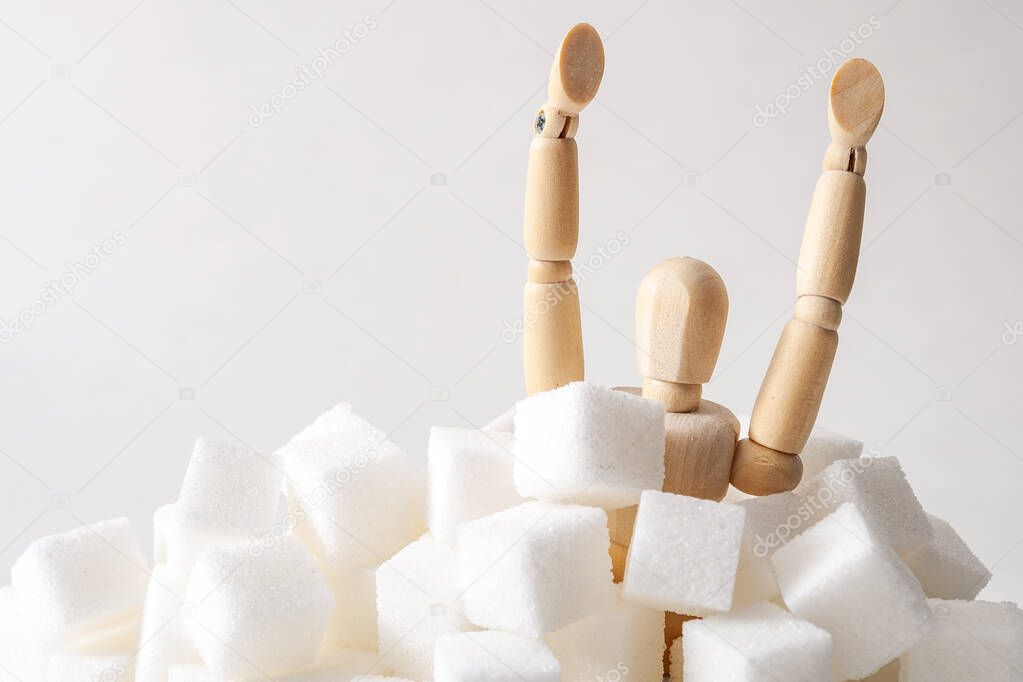 Sugar addiction, insulin resistance, unhealthy diet and November 14 is diabetes awareness day concept with a puppet drowning in sugar cubes isolated on white background and copy space for text