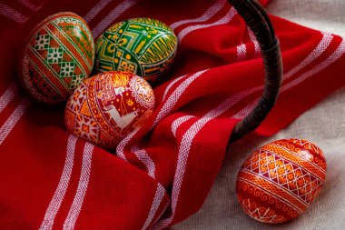 Bahar tatili ve doğu Avrupa 'ya özgü karmaşık ve karmaşık desenleri olan üç boyanmış yumurta ve her bir yumurtayla birlikte kırmızı kumaşlı eski bir hasır sepet ve kırmızı kumaşla mutlu paskalya konsepti.