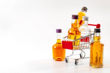 İçki almak, içki reyonundan alışveriş yapmak ve mini alkol şişeleri ile alkollü içecek konsepti temasını beyaz arka planda izole edilmiş küçük bir süpermarket arabasında satın almak.